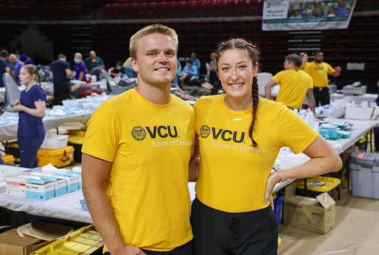 Two students in yellow VCU shirts smile in a large auditorium