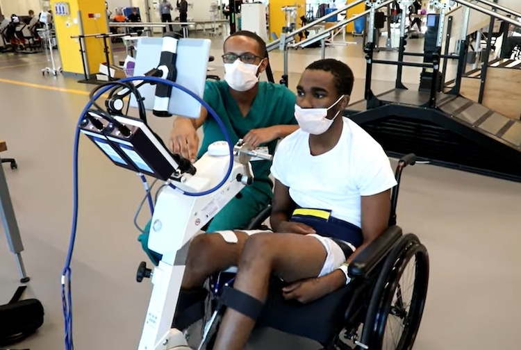 Patient sits in a wheelchair while reviewing documents on a computer with a health care provider.