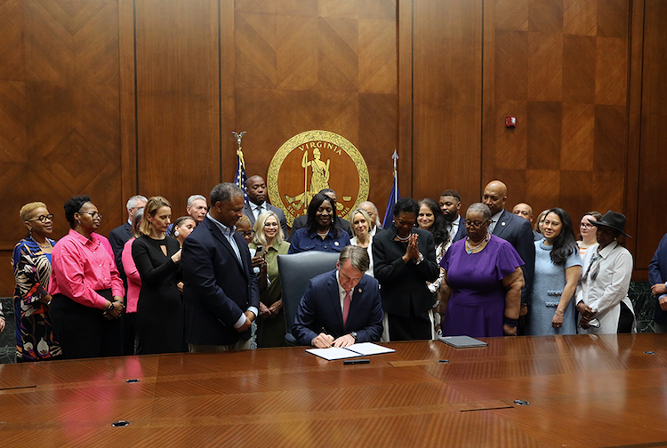 Group of people around governor while he signs a bill.