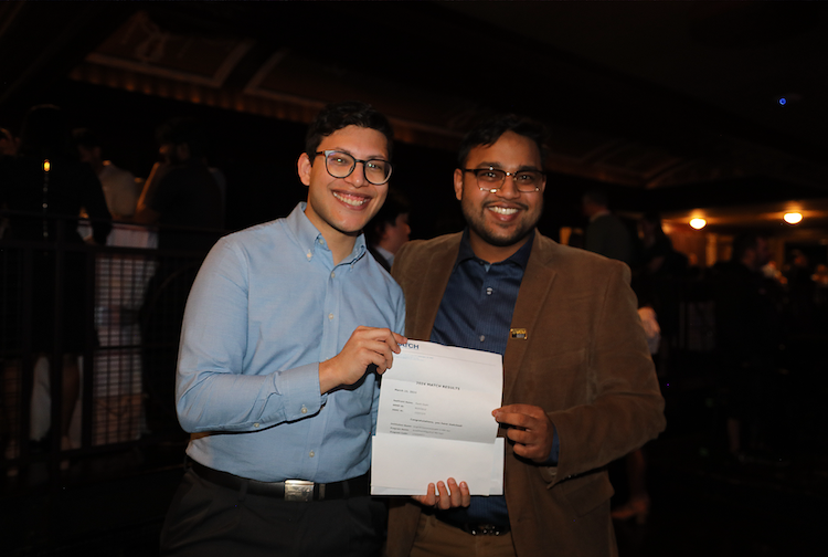 Two men in button down shirts stand with a residency program acceptance letter together