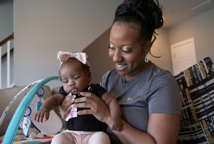 Woman holding baby on a couch. Baby has a pink bow in her hair.