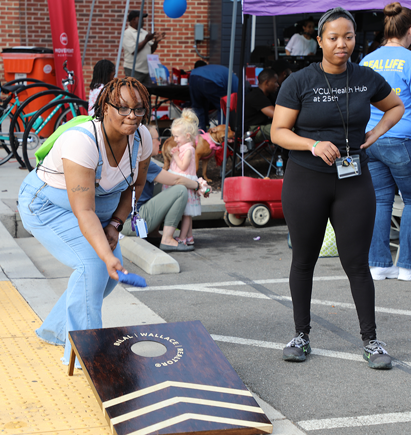 two women are playing corn hole outside in a parking lot.