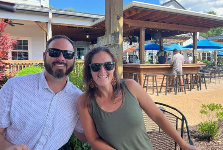 A couple sits smiling at a restaurant. On the left is Taryn Dwan, an athlete and cancer survivor