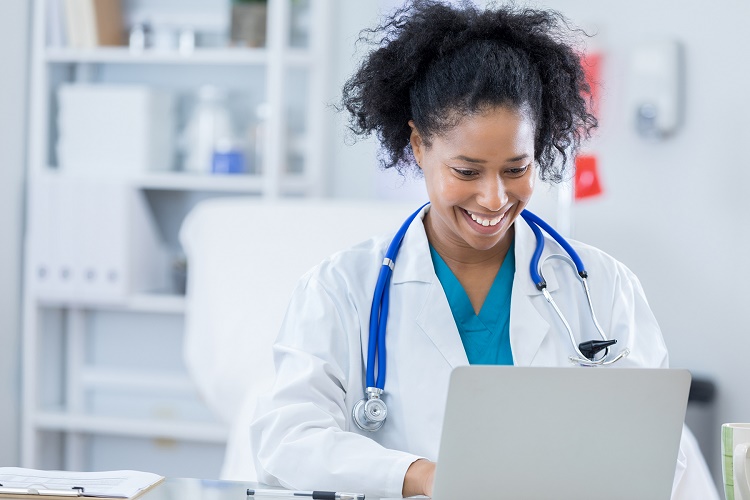 African-American female doctor smiling and looking down at laptop